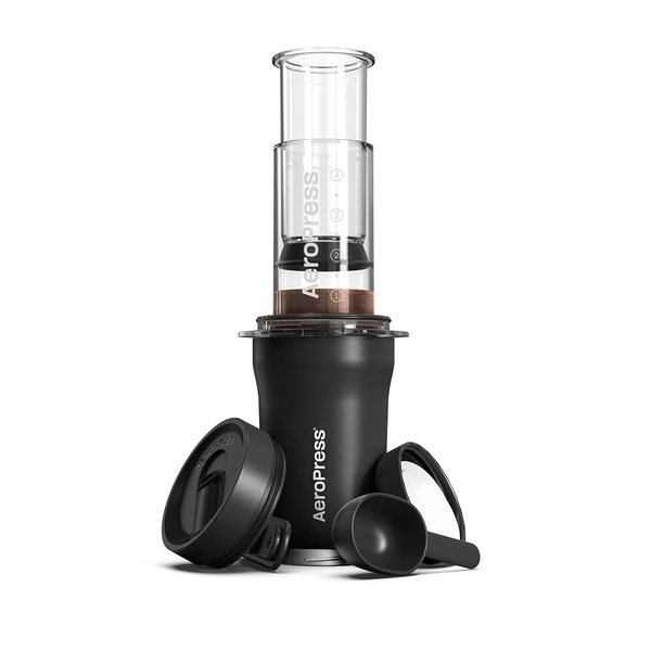 AeroPress Go Plus coffee maker with its components including the main chamber, plunger, filter cap, scoop, and stirrer. The AeroPress is shown assembled with coffee grounds inside.