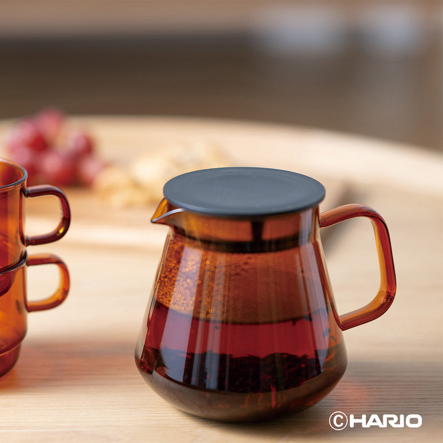 Amber glass coffee server with a lid on a wooden surface, featuring the Hario brand.