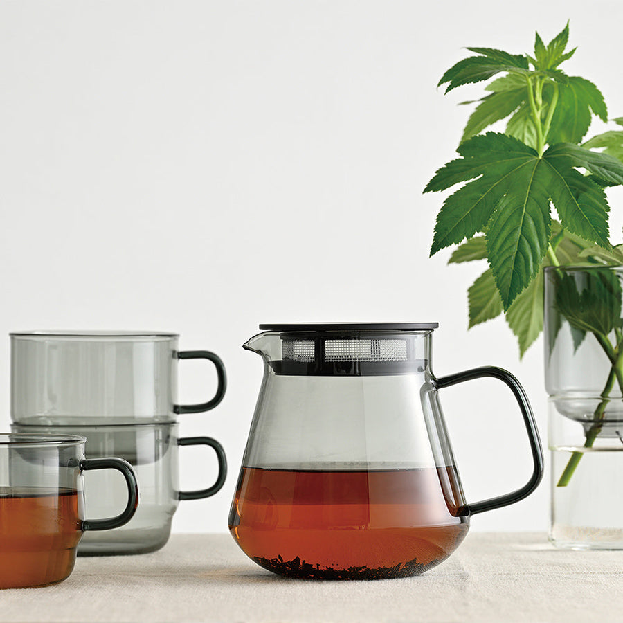 Tea set with teapot and cups on a white surface, featuring a cannabis plant.