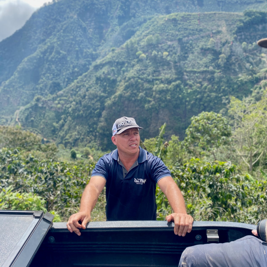 Pablo Bonilla stands by the side of his pickup truck with La Ladera farm in the background.