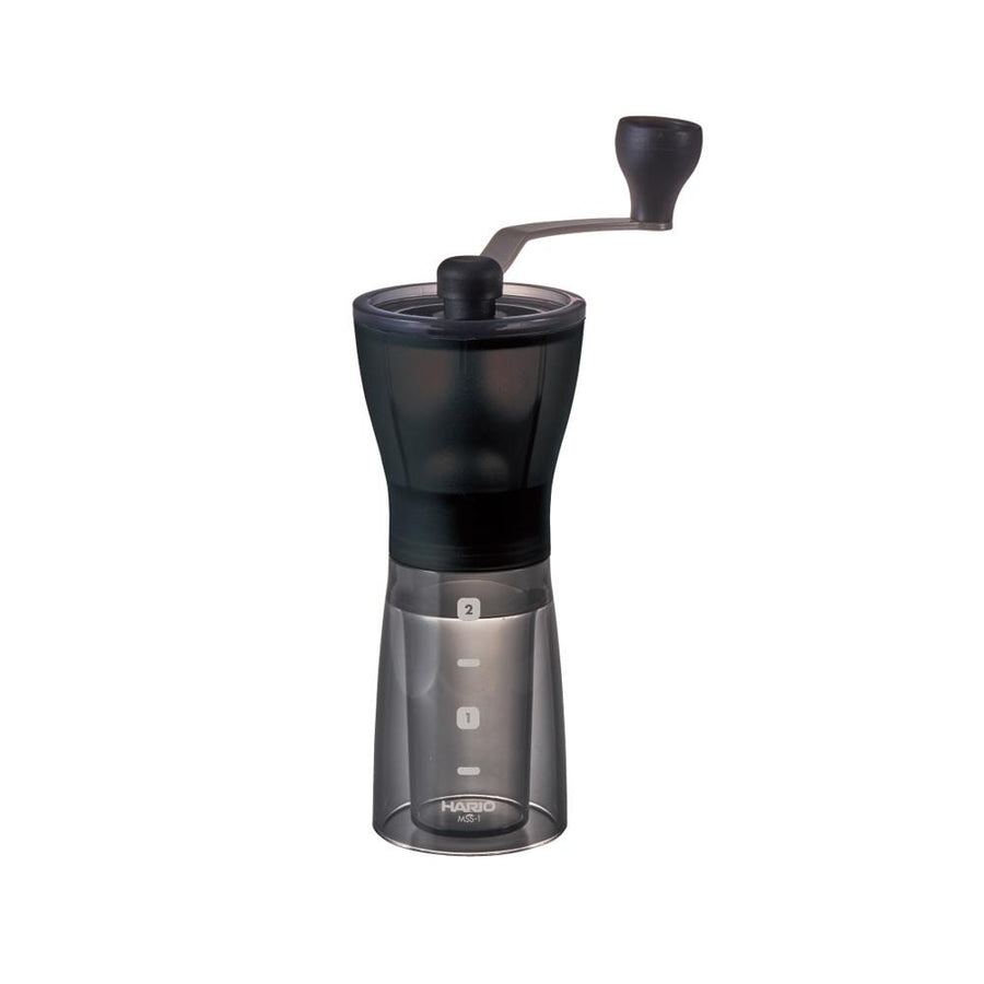 Hario Mini Mill PLUS manual coffee grinder with ceramic burrs, dark transparent body, and measurement markings for 1 and 2 cups.