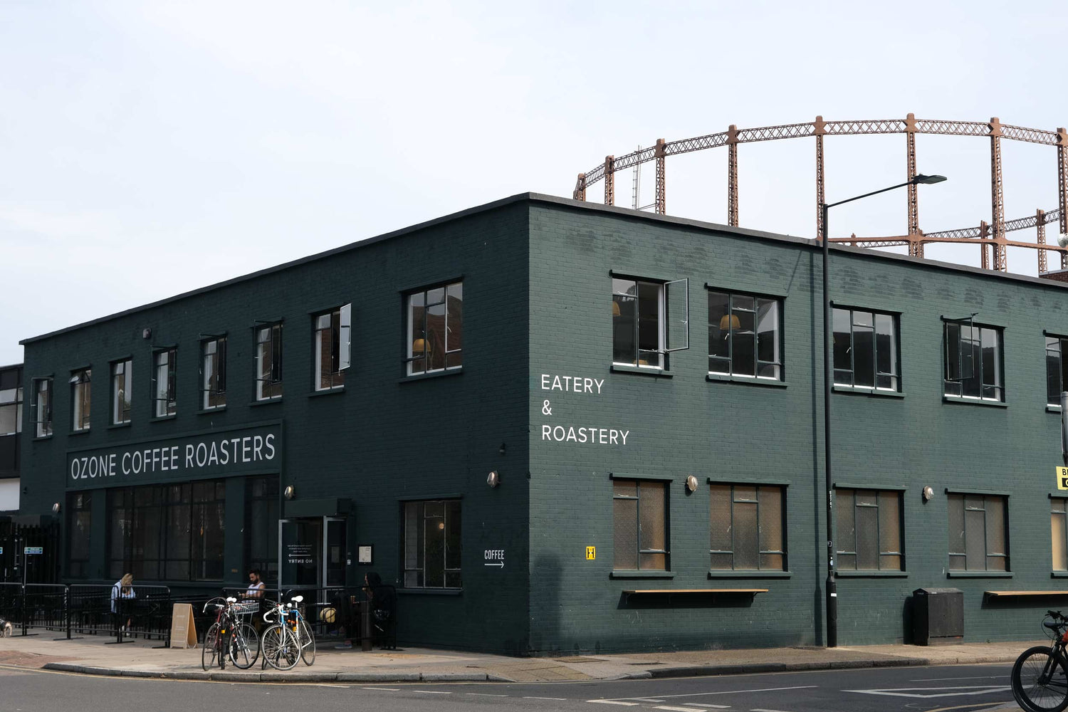 Ozone Coffee Roasters London Fields – dark green café exterior with outdoor seating, bikes, and gas holder backdrop.