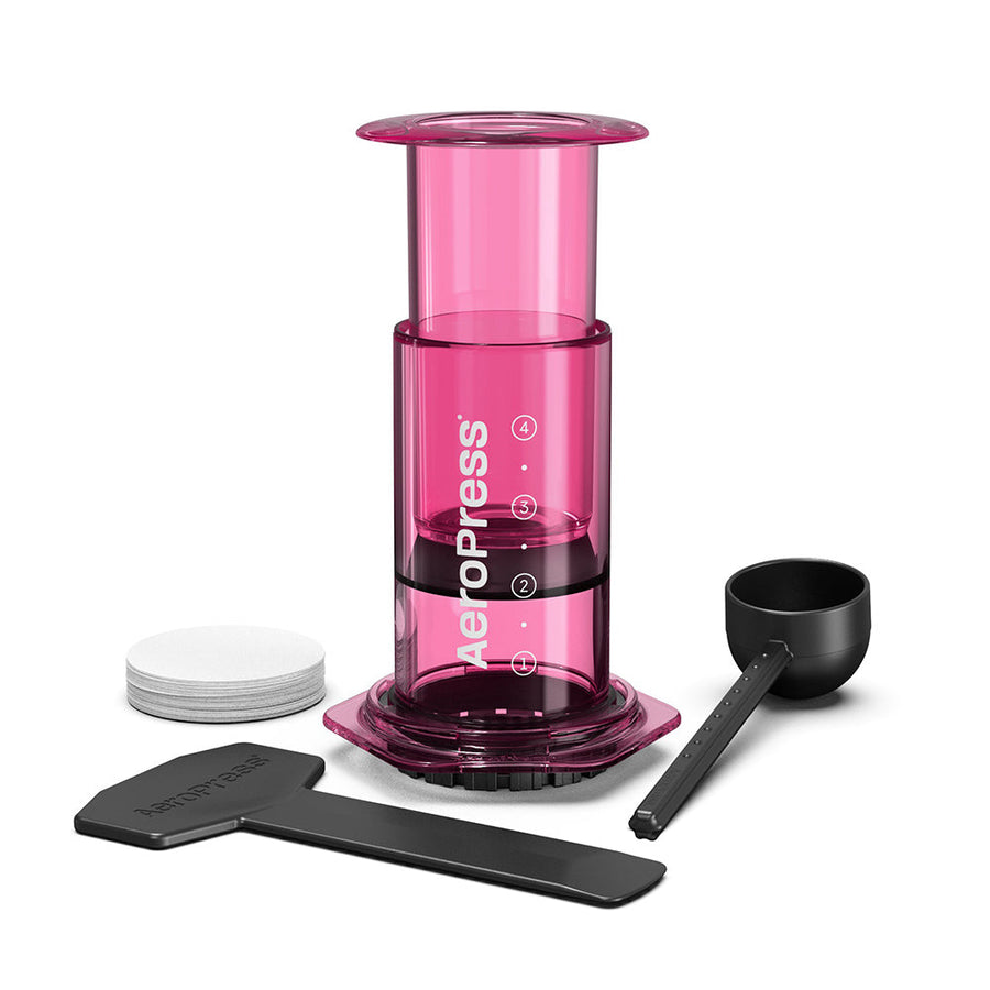 A pink AeroPress coffee maker made of shatterproof Tritan material, featuring a clear chamber, plunger, filter cap, and seal.