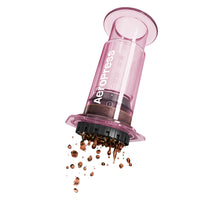 A pink AeroPress coffee maker made of shatterproof Tritan material, featuring a clear chamber, plunger, filter cap, and seal.