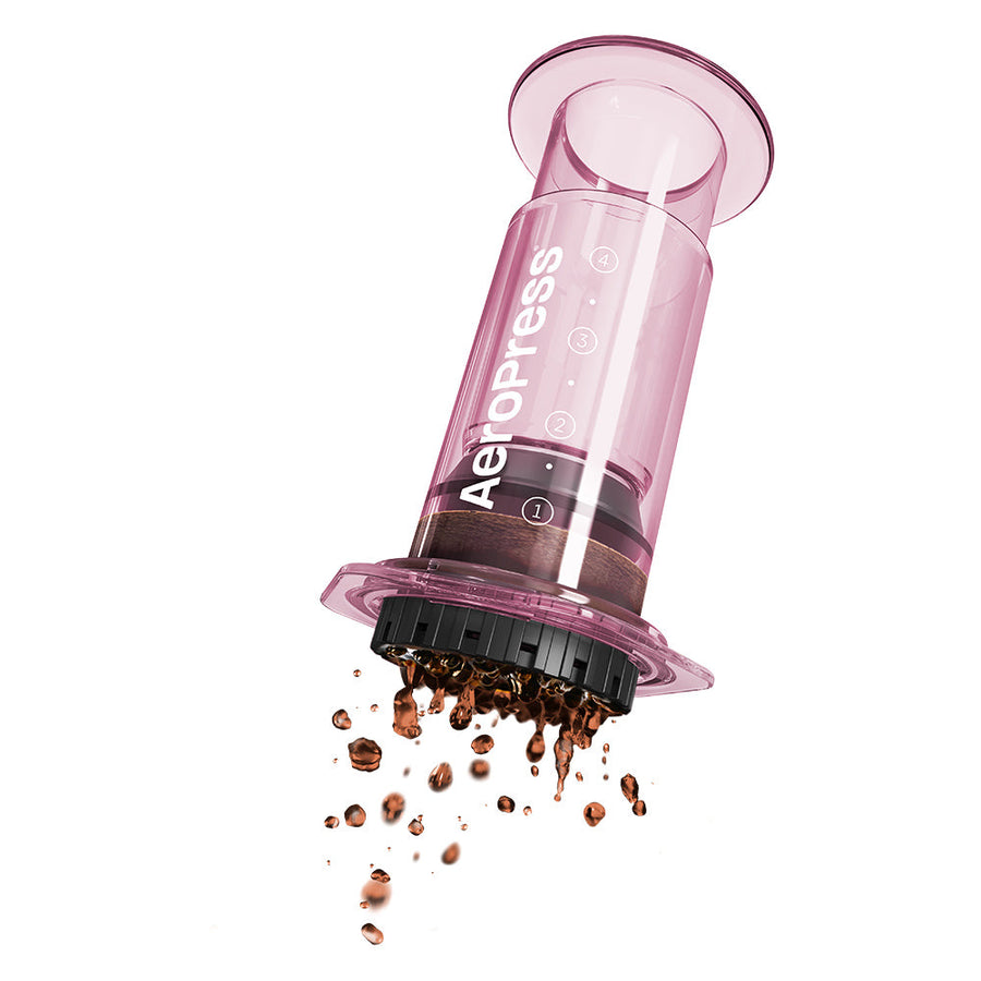 A pink AeroPress coffee maker made of shatterproof Tritan material, featuring a clear chamber, plunger, filter cap, and seal.