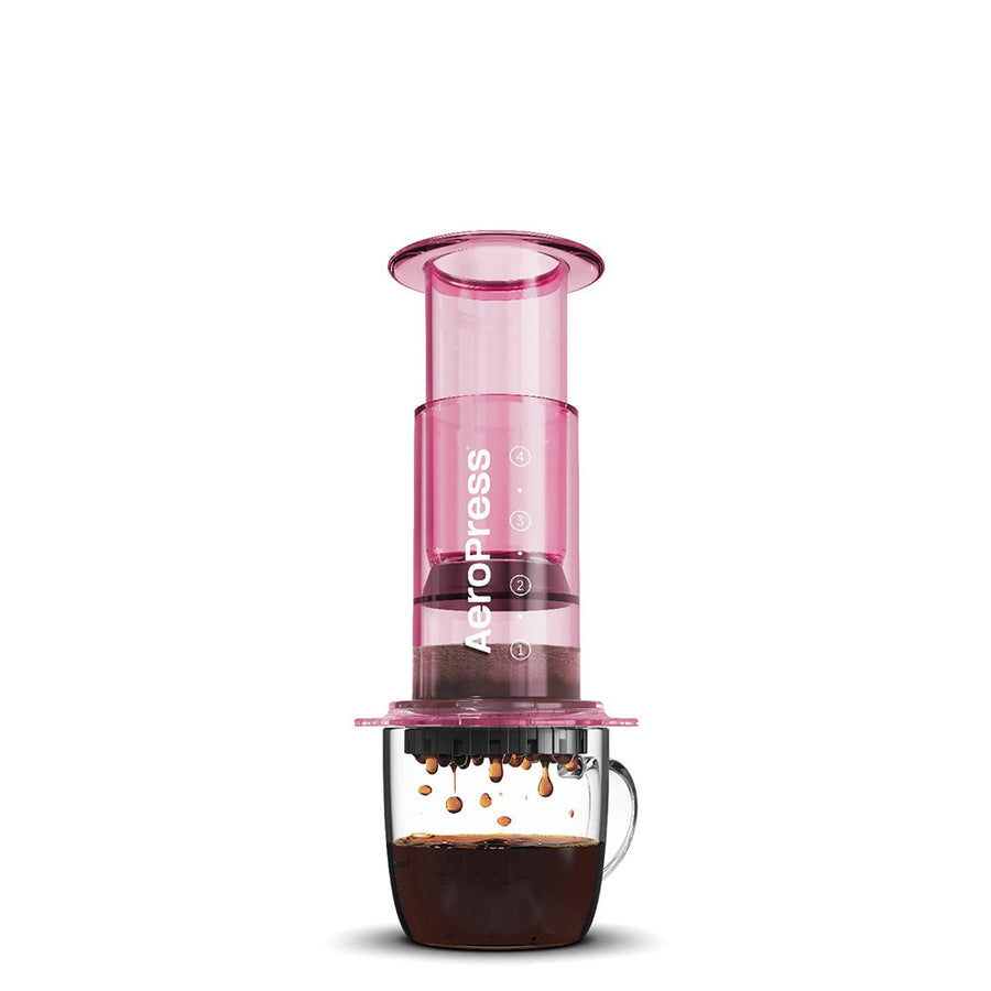 A pink AeroPress coffee maker made of shatterproof Tritan material, featuring a clear chamber, plunger, filter cap, and seal.