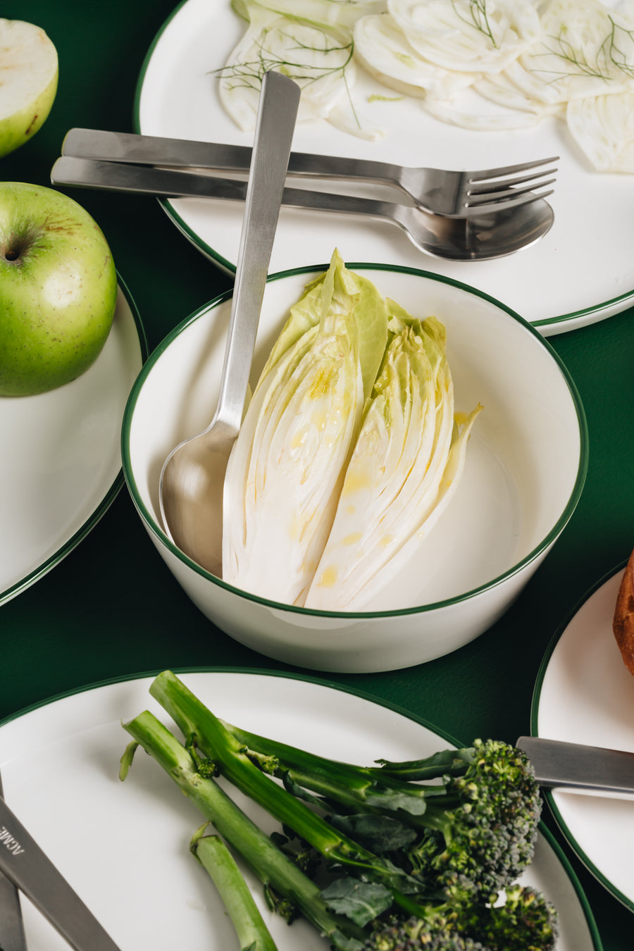White and green Acme tableware and flatware, some with food dishes, on a green surface