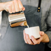 Fellow Eddy Steaming Pitcher - Polished Steel 12oz pouring milk into a cup in the hands of a barista