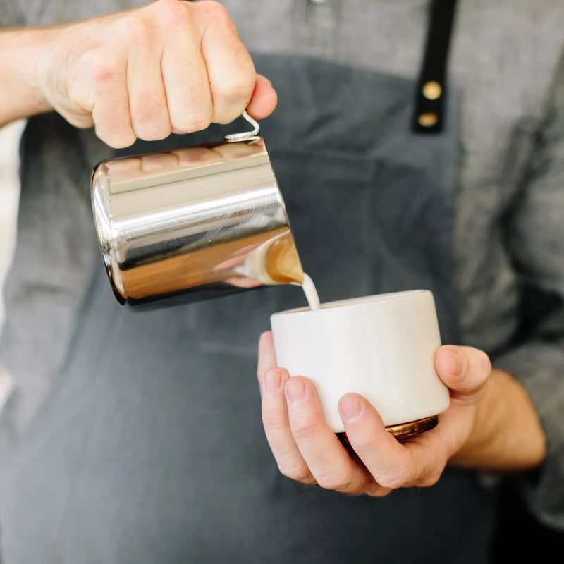Fellow Eddy Steaming Pitcher - Polished Steel 12oz pouring milk into a cup in the hands of a barista
