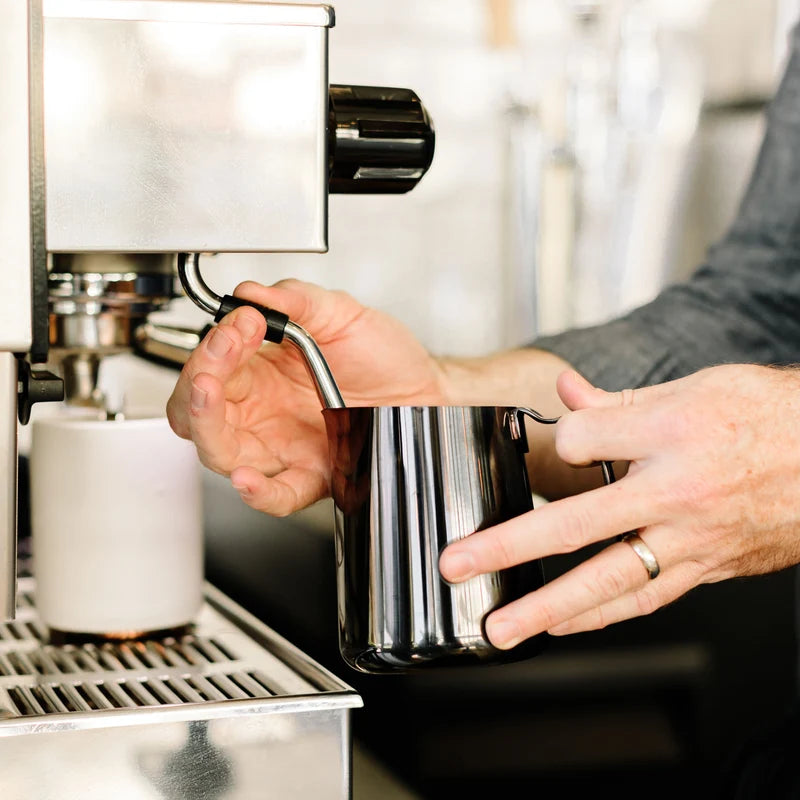 Fellow Eddy Steaming Pitcher - Polished Graphite 12oz steaming milk on a steam wand on a white espresso machine