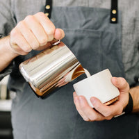 Fellow Eddy Steaming Pitcher - Polished Steel 18oz pouring milk into a coffee cup in the hands of a barista