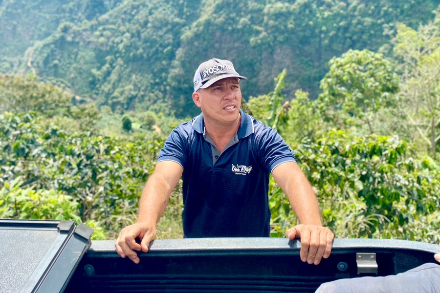 Pablo Bonilla, owner of the Don Mayo micromill, stands by the side of his pickup truck with La Ladera farm in the background.