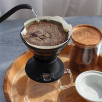 Coffee being brewed with a pour-over coffee maker Hario Switch V60 Immersion Dripper on a wooden tray.