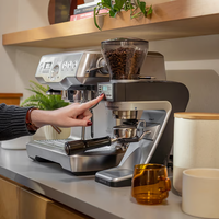 Person using a coffee machine on a kitchen counter with cups and a plant in the background and a Baratza Sette 270Wi Coffee Grinder