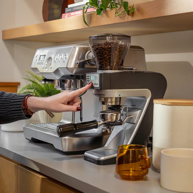 Person using a coffee machine on a kitchen counter with cups and a plant in the background and a Baratza Sette 270Wi Coffee Grinder